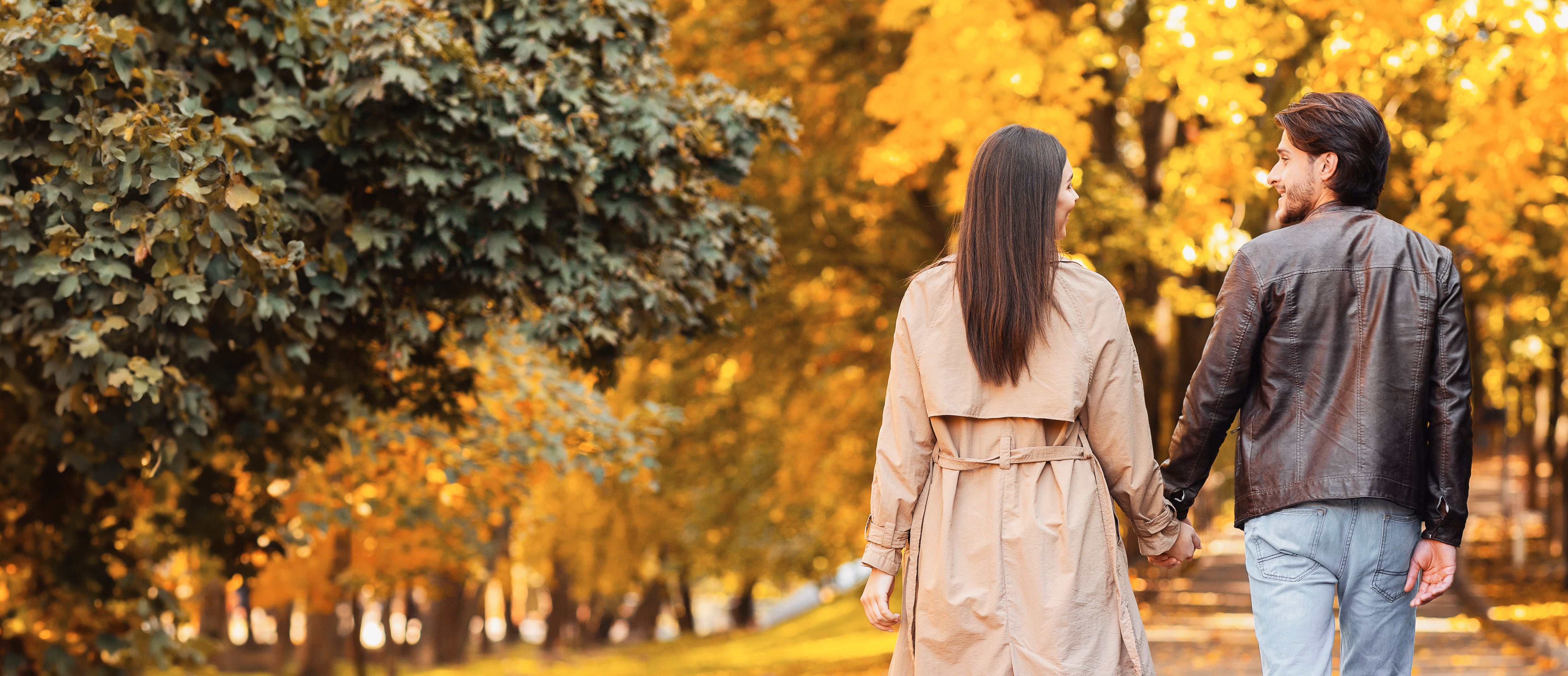 Paar spaziert im Herbst durch einen Wald, umgeben von warmen Farben und fallendem Laub, symbolisiert Nähe und gemeinsame Zeit.
