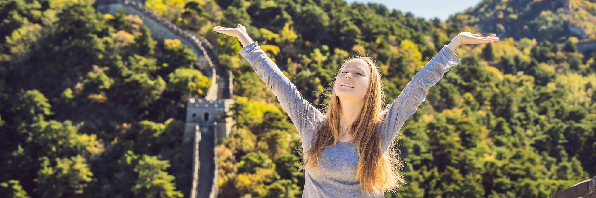 Glückliche Frau hebt die Arme auf chinesischer Mauer
